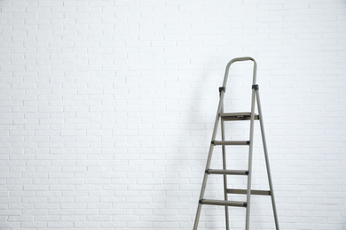 Photo of Metal stepladder near white brick wall. Space for text