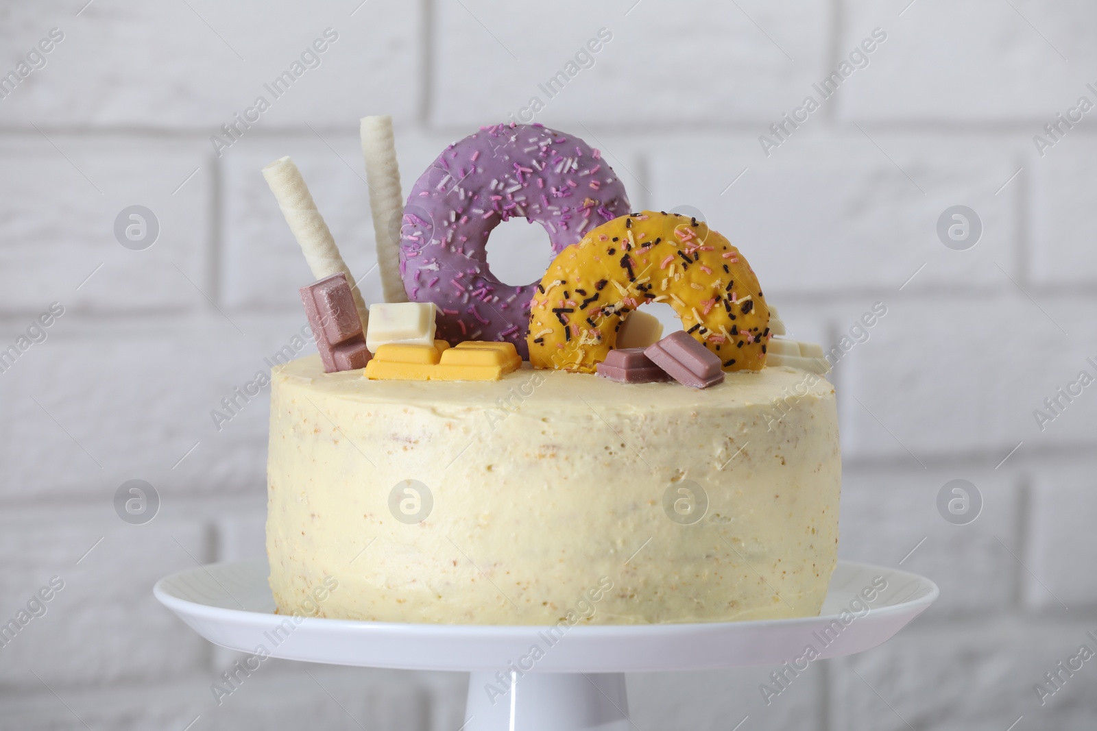 Photo of Delicious cake decorated with sweets against white brick, closeup