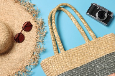Photo of Wicker beach bag, straw hat, sunglasses and camera on light blue background, flat lay