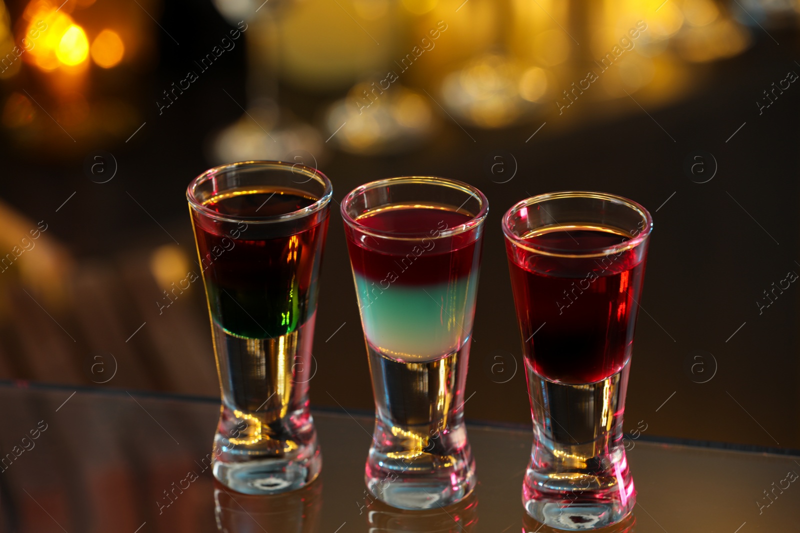 Photo of Different shooters in shot glasses on surface against blurred background Alcohol drink