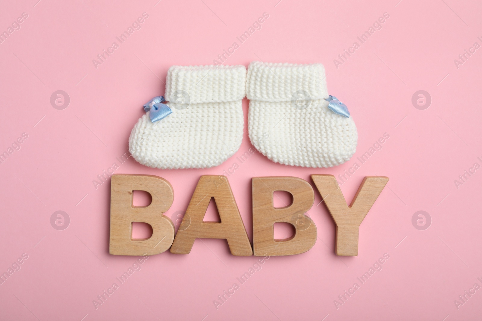 Photo of Flat lay composition with child's booties and word Baby on pink background
