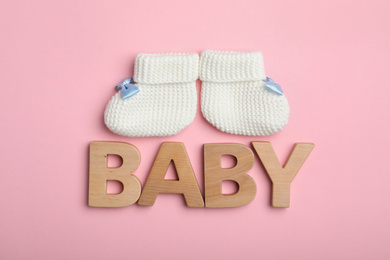 Photo of Flat lay composition with child's booties and word Baby on pink background