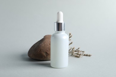 Bottle with cosmetic serum, stone and dry flowers on light grey background