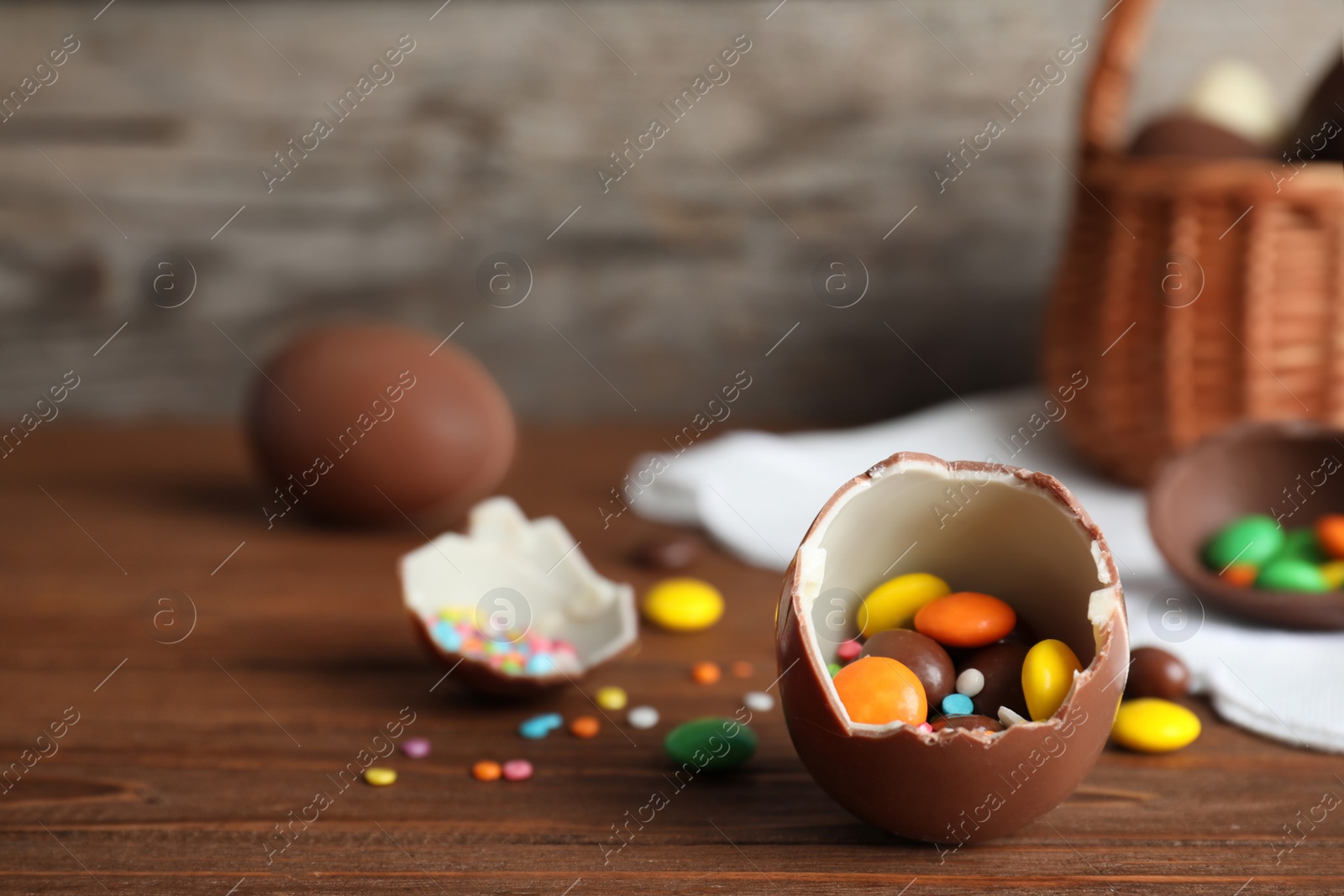 Photo of Broken chocolate Easter egg with candies on wooden table. Space for text