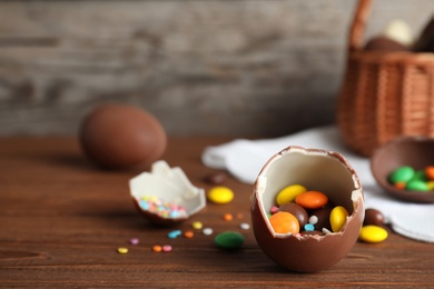 Photo of Broken chocolate Easter egg with candies on wooden table. Space for text