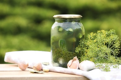 Photo of Jar of delicious pickled cucumbers and ingredients on wooden table against blurred background. Space for text