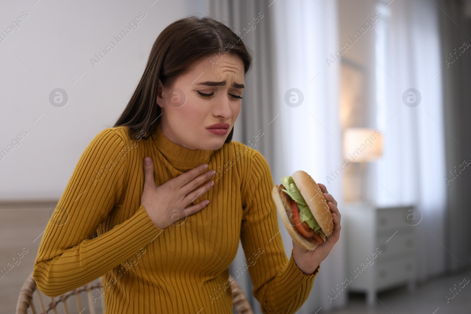 Photo of Young woman suffering from nausea while eating burger at home