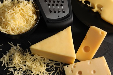 Photo of Grated, cut cheese and grater on black table, above view