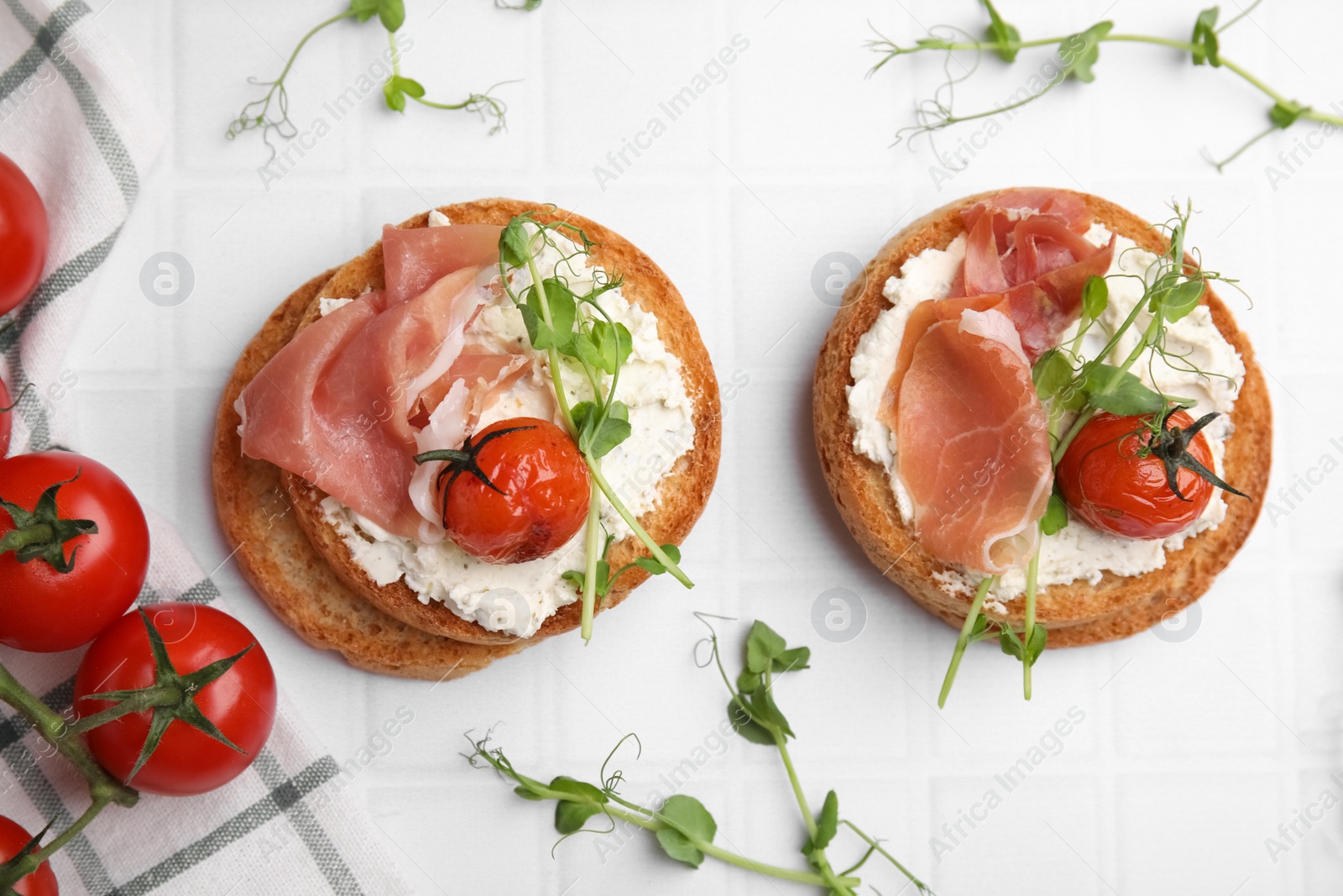 Photo of Tasty rusks with prosciutto, cream cheese and tomatoes on white table, flat lay