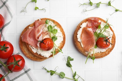 Photo of Tasty rusks with prosciutto, cream cheese and tomatoes on white table, flat lay