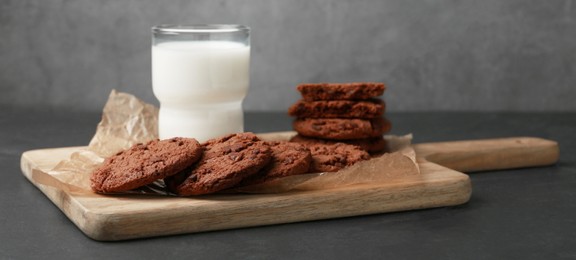 Photo of Board with tasty chocolate cookies and glass of milk on dark table. Space for text