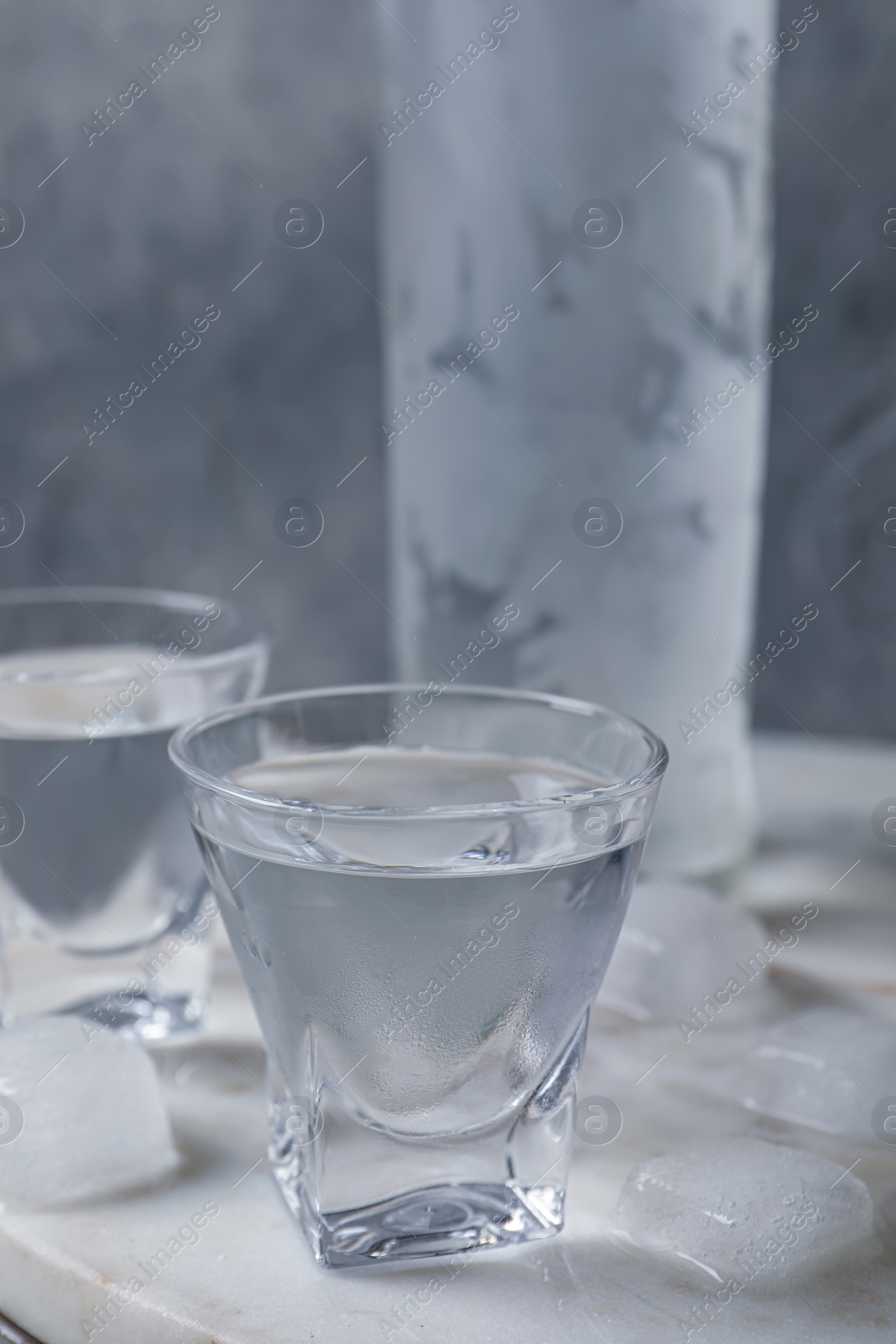 Photo of Shot glasses and bottle of vodka with ice cubes on table