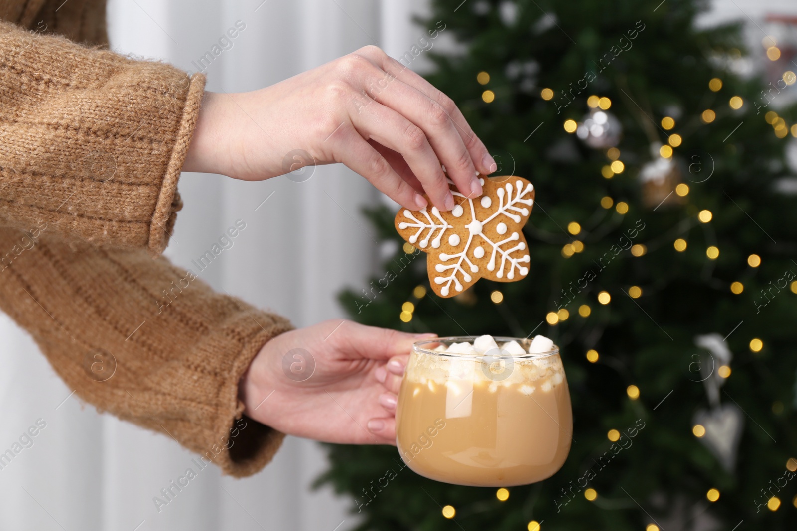 Photo of Woman with decorated cookie and cup of cocoa near Christmas tree, closeup