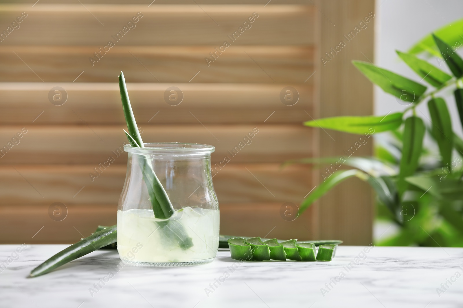 Photo of Jar with aloe vera gel and green leaves on table against blurred background. Space for text