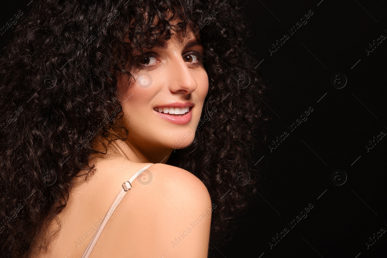 Photo of Beautiful young woman with long curly hair on black background. Space for text
