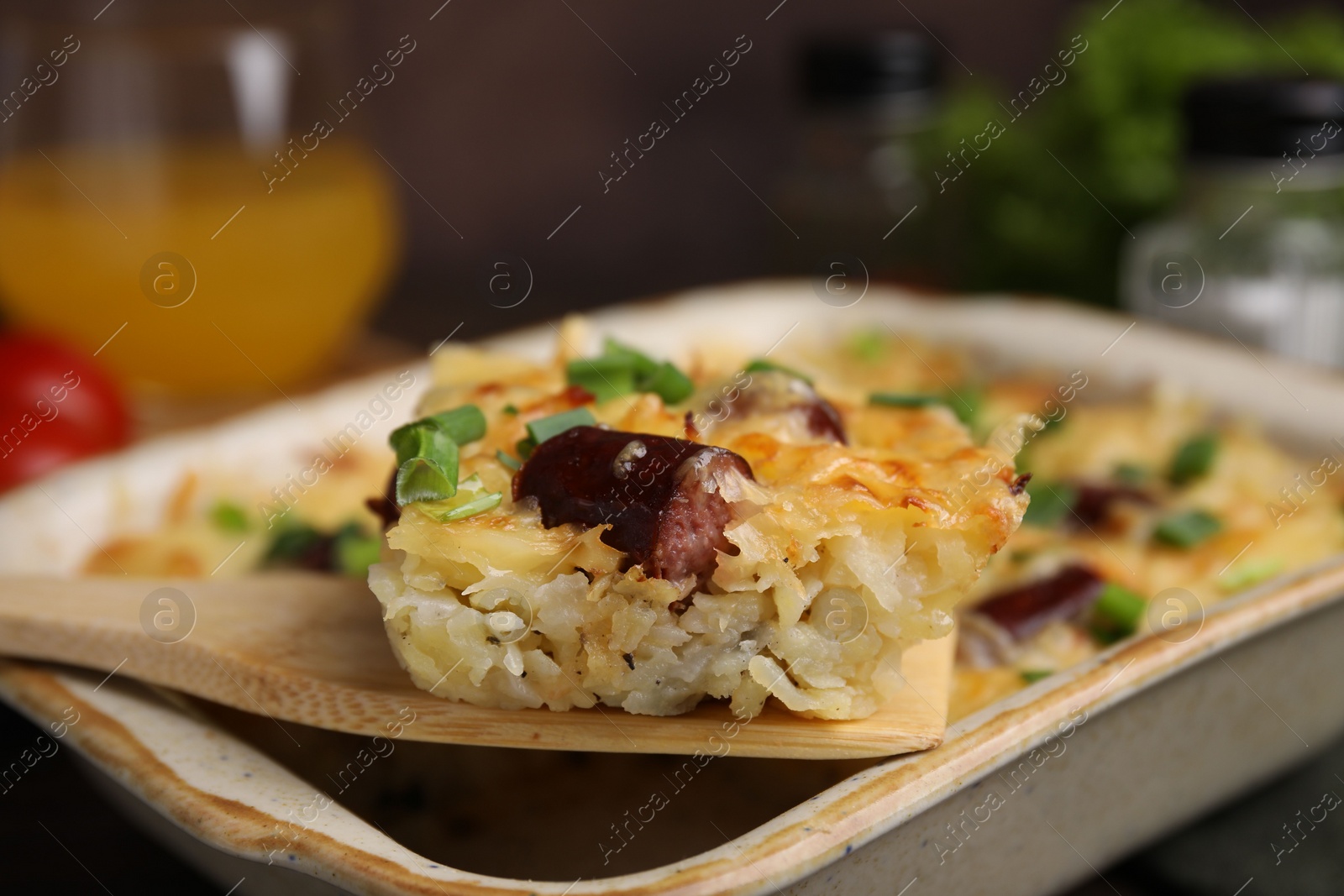 Photo of Taking piece of tasty sausage casserole from baking dish at table, closeup