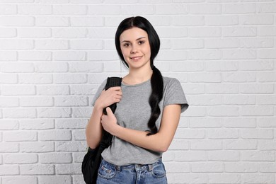 Photo of Smiling student with backpack near white brick wall