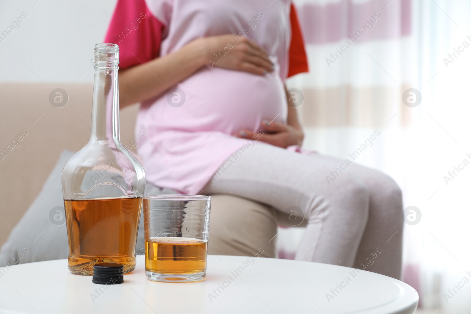 Photo of Future mother at home, focus on bottle and glass with alcohol drink. Bad habits during pregnancy