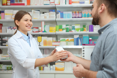 Image of Professional pharmacist giving medicine to customer in modern drugstore