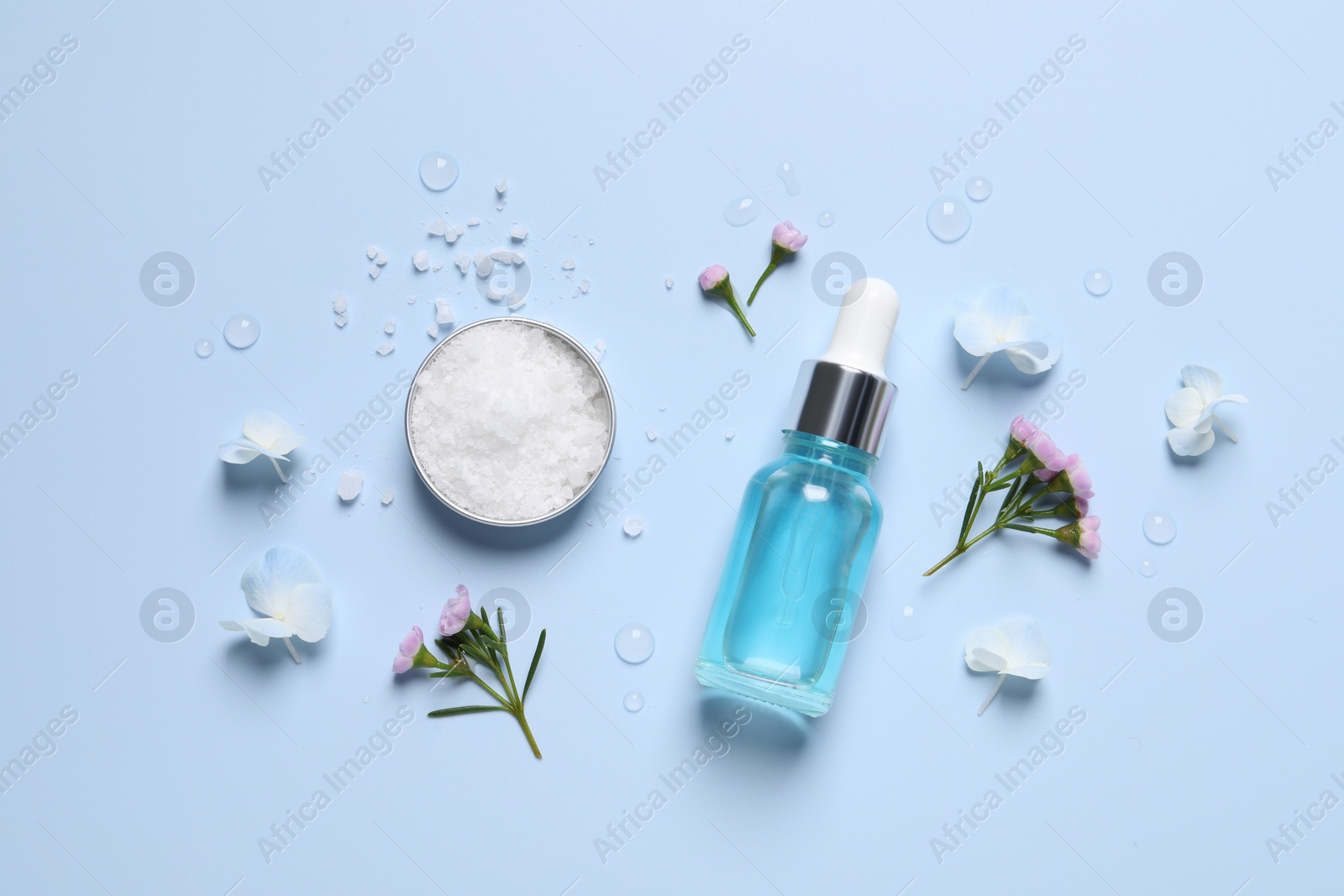 Photo of Bottle of cosmetic serum, beautiful flowers and sea salt on light blue background, flat lay