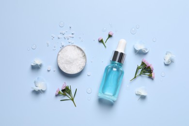 Bottle of cosmetic serum, beautiful flowers and sea salt on light blue background, flat lay