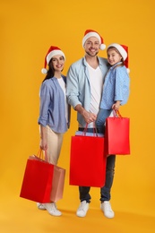 Photo of Happy family with paper bags on yellow background. Christmas shopping