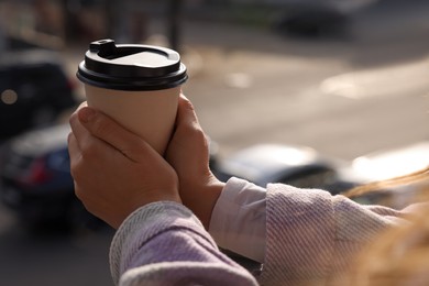 Woman holding paper coffee cup outdoors, closeup