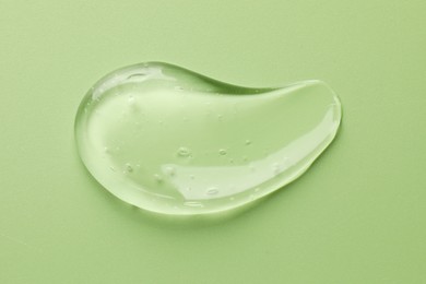 Smear of clear cosmetic gel on light green background, top view