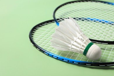 Feather badminton shuttlecock and rackets on green background, closeup. Space for text