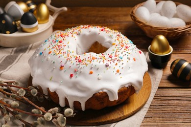 Photo of Delicious Easter cake decorated with sprinkles near eggs and willow branches on wooden table, closeup