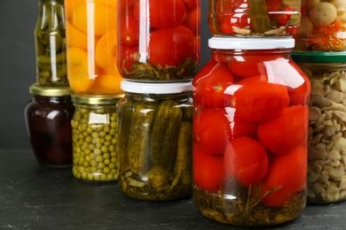 Photo of Jars of pickled vegetables on grey table, closeup