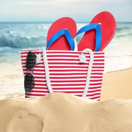 Image of Stylish striped bag and other beach accessories on sand near sea