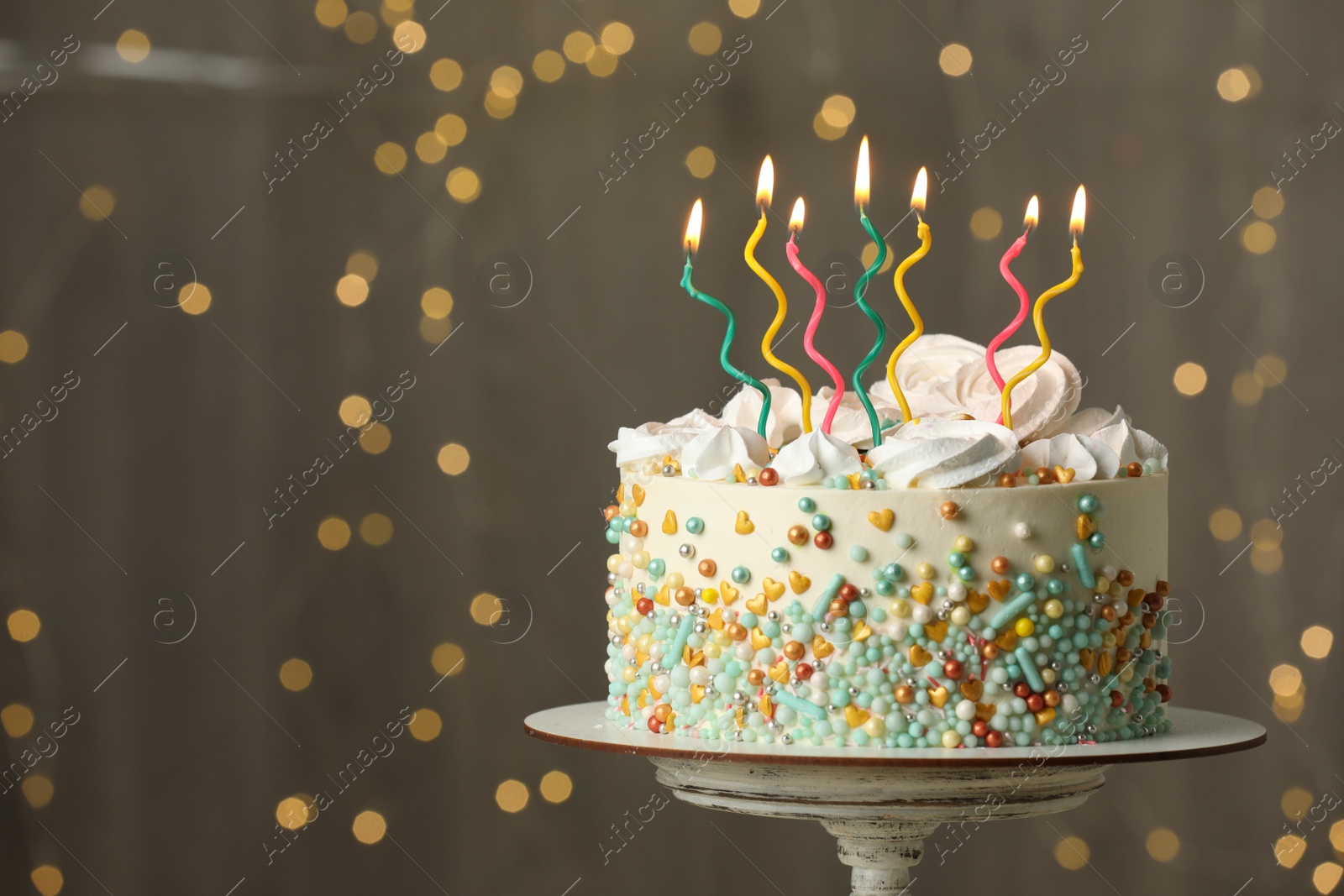 Photo of Beautiful birthday cake with burning candles on stand against festive lights. Space for text