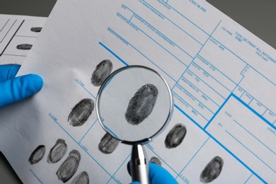 Photo of Criminalist studying fingerprints with magnifying glass, closeup