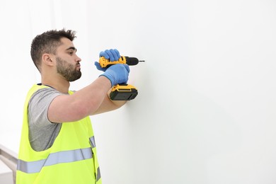 Young worker in uniform using electric drill indoors. Space for text