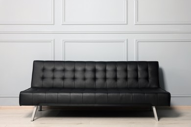 Stylish leather sofa near white wall in room. Interior design