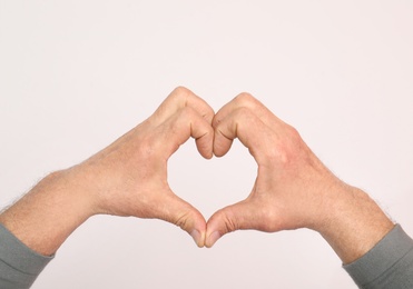 Photo of Senior man making heart with his hands on white background, closeup
