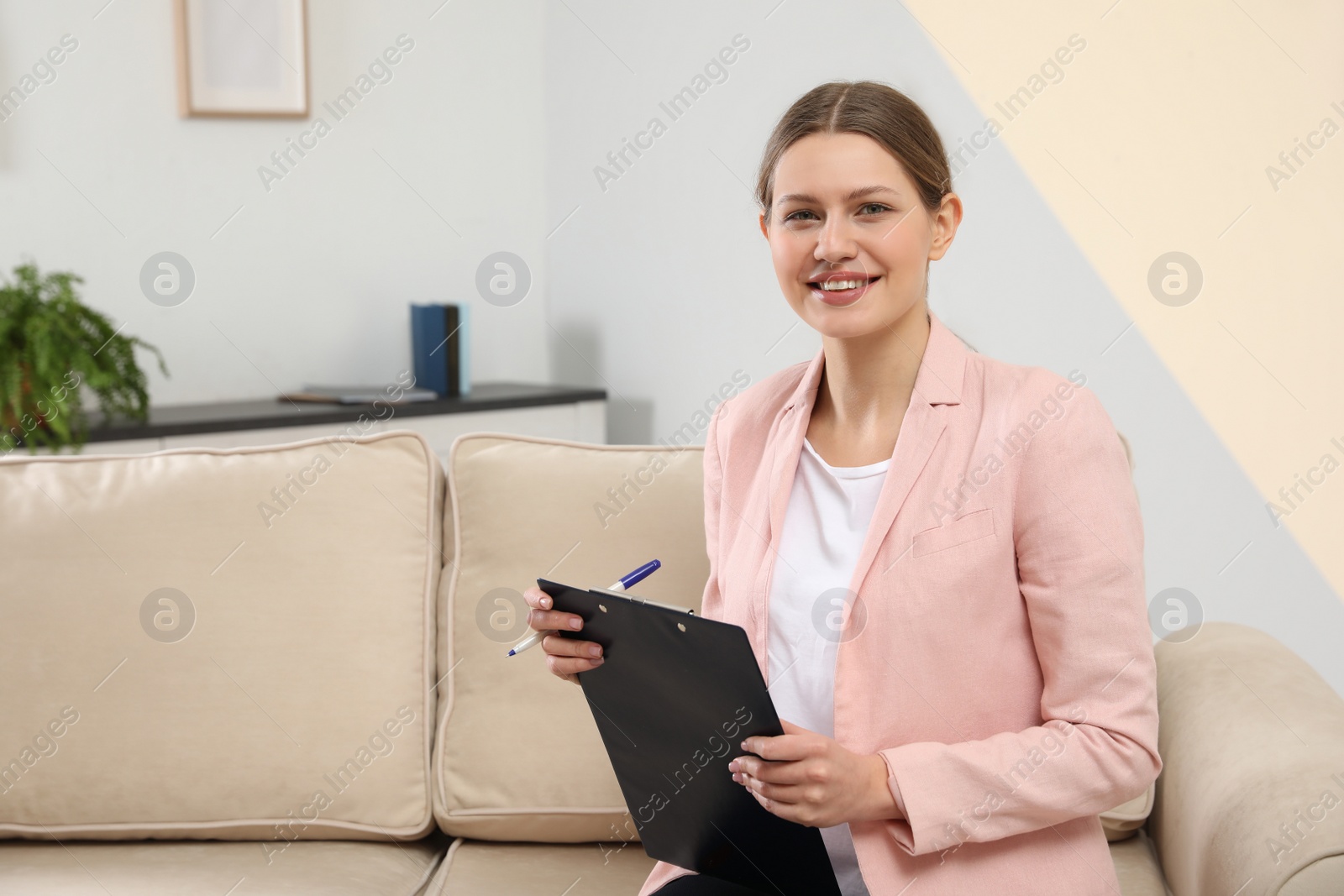 Photo of Professional psychotherapist with clipboard on sofa in office