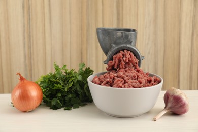 Photo of Mincing beef with manual meat grinder. Parsley, garlic and onion on white wooden table