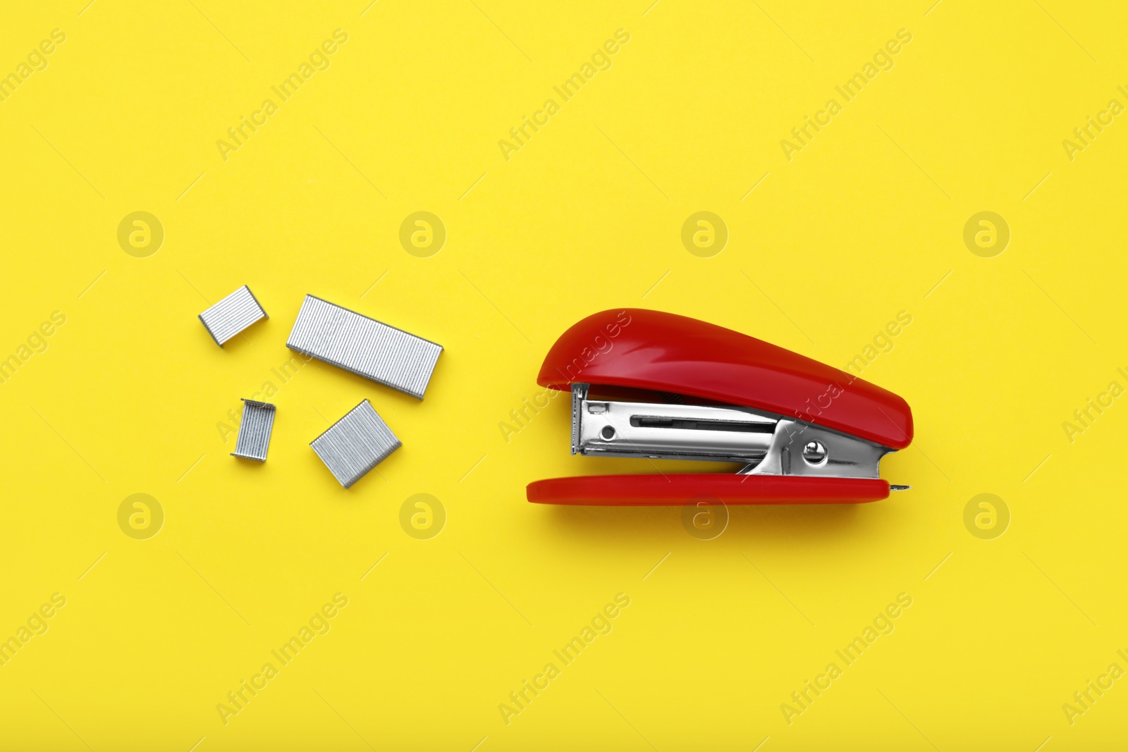 Photo of New bright stapler with staples on yellow background, fat lay. School stationery