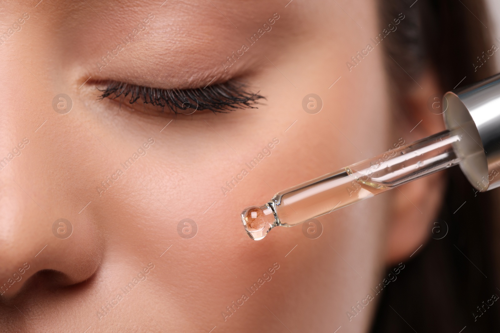 Photo of Young woman applying essential oil onto face, closeup