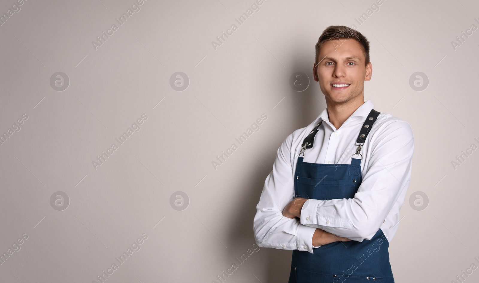 Photo of Portrait of happy young waiter in uniform on light background