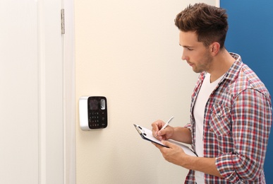 Photo of Young man checking security alarm system indoors