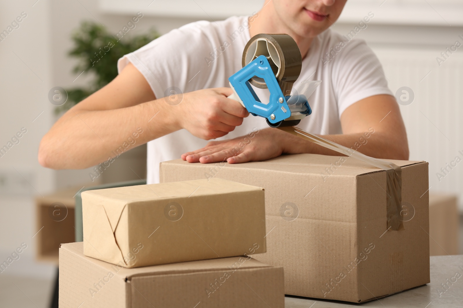 Photo of Man packing box with adhesive tape indoors, closeup