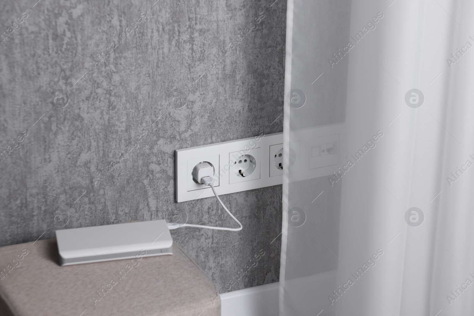 Photo of Power bank plugged into electric socket on grey wall