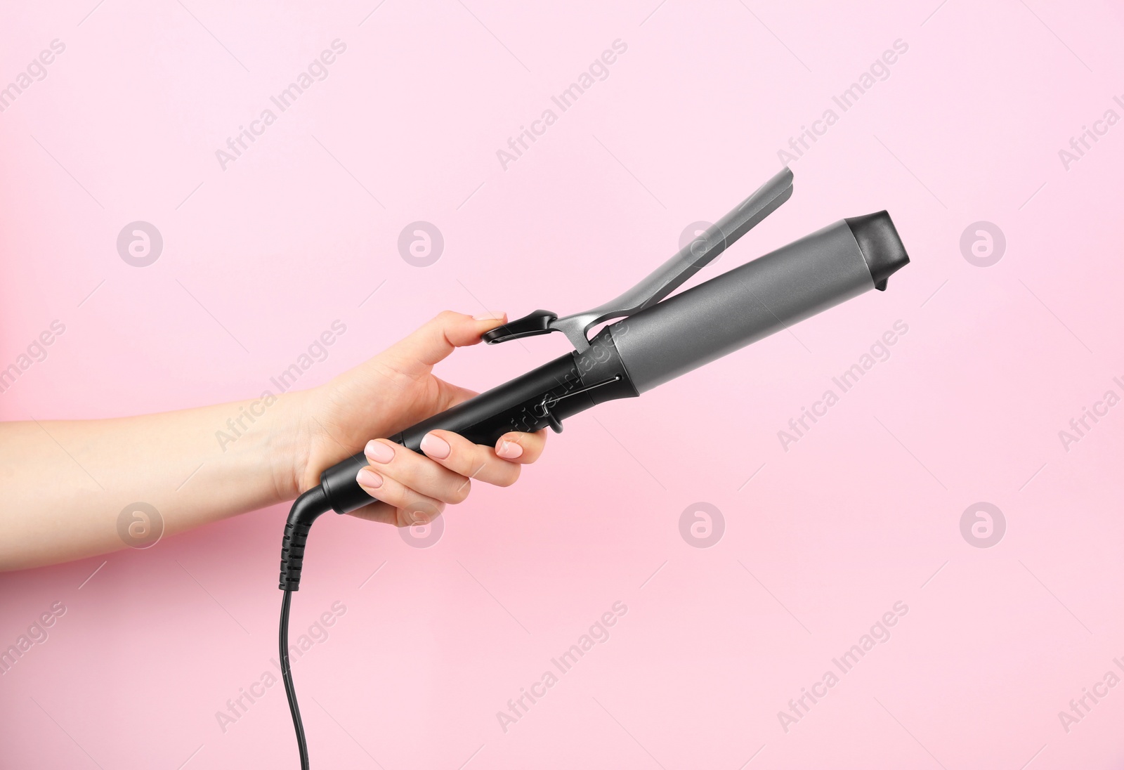 Photo of Hair styling appliance. Woman holding curling iron on pink background, closeup