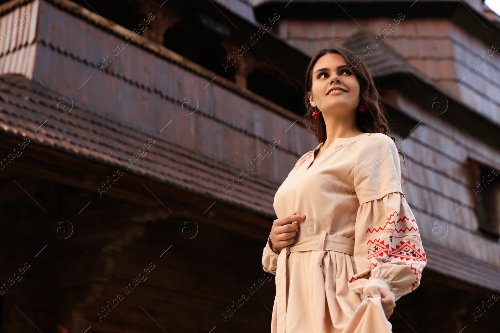 Photo of Beautiful woman wearing embroidered dress near old wooden church in village. Ukrainian national clothes