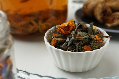 Photo of Dry herbal tea in bowl on tray, closeup