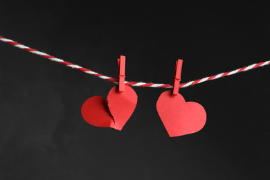 Photo of Broken and whole red paper hearts on rope against black background. Relationship problems concept