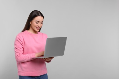 Photo of Smiling young woman working with laptop on grey background, space for text